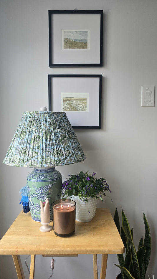 Lamp on a wooden table with framed pictures above, against a gray wall.