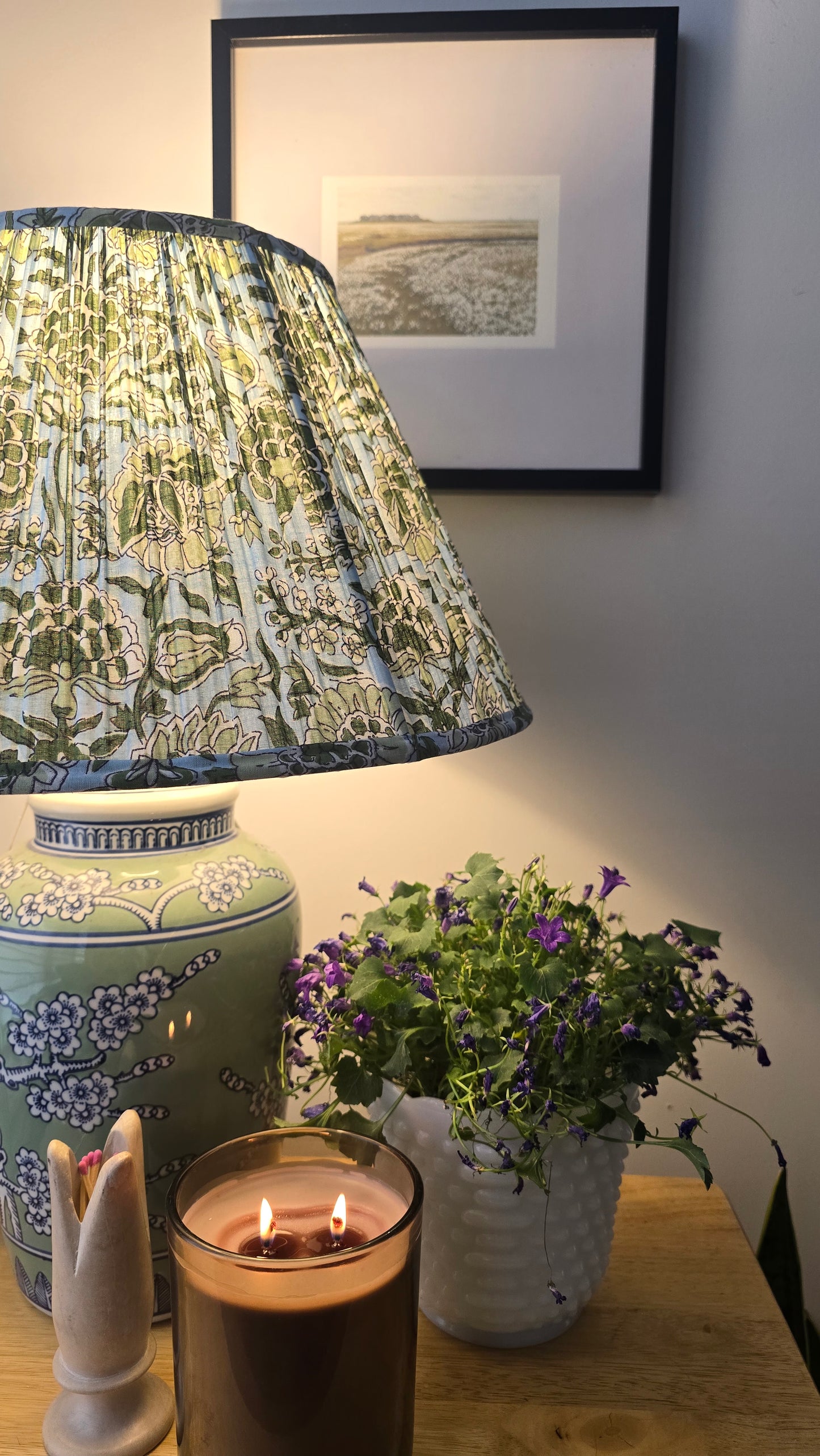 Decorative lamp with patterned shade, candle, and plant on a table.